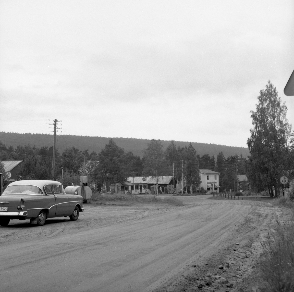 Bilden föreställer infarten till Värnäs från väg E45/E16. Rakt fram ser man BP-macken ägd av Olof Persson. Det stora vita huset inhyste Kooperativa Förbundets affär (Konsum), Koppra i folkmun. Förestods av Ragnhild Persson. Från slutet av 1950-talet: Värnäs, Stöllet. 