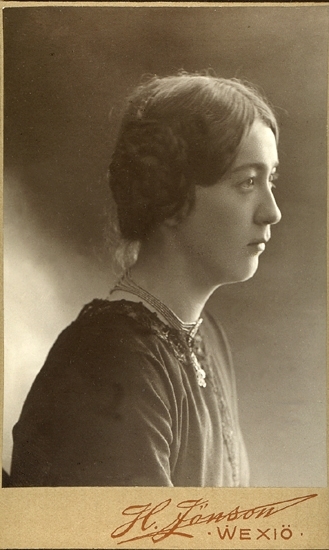 Porträttfoto (bröstbild) en okänd ung kvinna i profil. 
Hon har klänning och ett tättsittande halsband på sig.