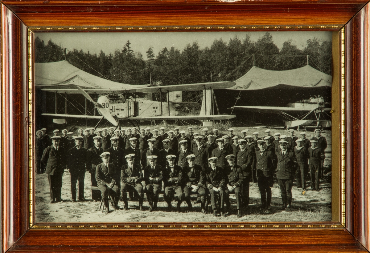 Gruppfotografi. Marinpersonal samlade framför två marina flygplan vid kustflottans flygstation vid Hårsfjärden år 1924. Inramat foto.