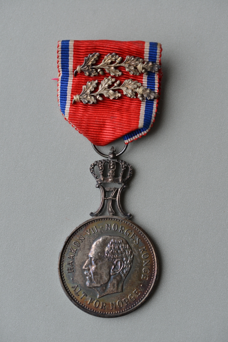 Kong Haakon VII i profil. Monogrammet til KongHaakon VII. På baksida kors og to økser.