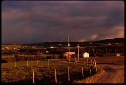 Landskap med regnbuer  og svarte skyer, uvær brygger opp.