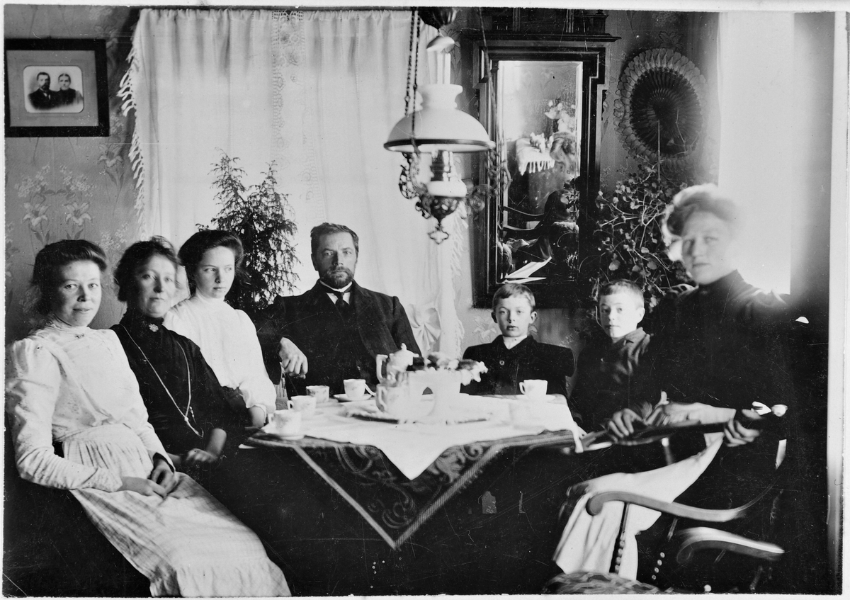 Familiegruppe rundt kaffebordet, med gitarspillende dame.
