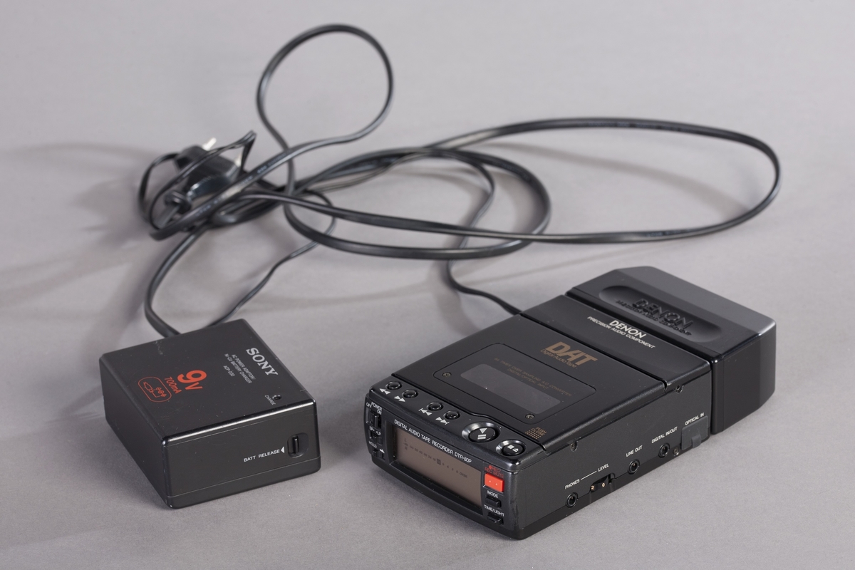 Bærbar og kompakt DAT-spiller i svart innretning med separat batteriholder og strømforsyning. Spilleren har innebygd mikrofonforsterker (analog inngang). I esken 1/2 finnes også bruksanvisning, 6 kassettbånd og en perm med foto og sanglister. Strømadapter finnes i eske 2/2.