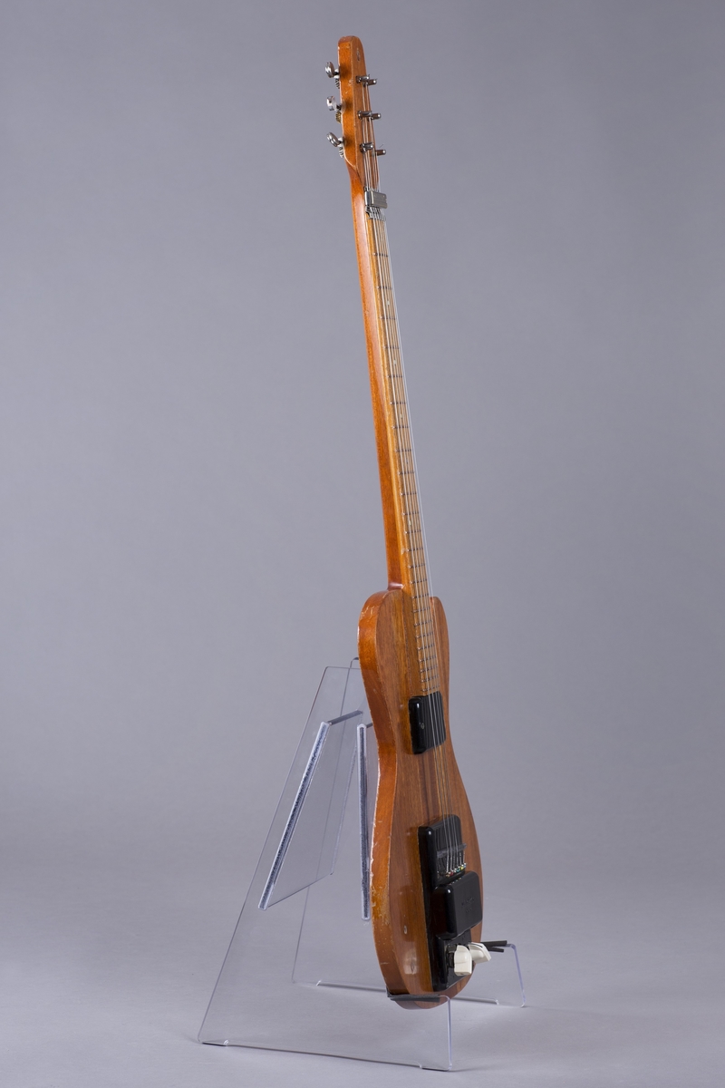 Elektrisk gitar med kropp og hals av mahogny. Magnet ved halsfeste og pickup ved strengefeste (NilsensSystem). Kontrollere for tilpasning og klangfarge. Tilpasning tilsvarer volum og gir størst volum på nivå 1. Enkelte av stemmeskruene er ikke originale.