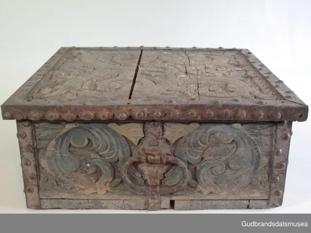 "Bladformer, smøygde band og drageornamentikk. Millom kantjarn og utskurden hev lokket fint utskorne små blad og halvrunde aggar. Vel vedlikehalde, sterk jarning og prydelege gangjarn. Truleg frå 1500 talet. Fra Haugen, Øystre Gausdal". (Jf. "Katalog for Lom Bygdesamling,1925).
Skrinrammen er holdt sammen av utvendige hjørnekantbeslag; jernhandtak i hver side. Fronten har nøkkelhullslås med beslag rundt. Lokket er satt samen av 2 bord, forsterket med jernbeslag rundt kanter på overside; to hengselbeslag festet til innside av lokk og bakstykke. Skrinsider blir holdt sammen av beslag ned langs hjørnekanter; har jernhandtak festet på jernbeslag.
Bunnen er satt sammen av 2 bord, festet til hverandre med to forsenka treplugger; bunnen var opprinnelig festet til underkant av skrinsider med 4 x 4 trenagler,seinere festet med spiker. 
Det er jernbeslag  på bakstykket midt, rundt hjørnekanter, omkring nøkkelhullslås, rundt lokk samt 2 handtak med beslag. Alle beslag er festet med store jernnagler; beslag på sidestykker er festet med små jernnagler under skrinbunnen. 3 av 8 bunnfester for beslag er fortsatt intakte.
DEKOR. De store jernnaglene med forskjøvet plassering på beslag ble sannsynligvis brukt som dekorelement; runde beslag på sider, bakstykke og front. Flatskurd på lokk med flettet, stilisert renessanseranke, der bladverk er "omgjort" til småspiraler eller rundinger.  På skrinsidene akantusskurd med c-former, bladtunger uten stilk og naturalistiske småblad i rokokkostil. Flatskurd var vanlig i Gudbrandsdalen i perioden ca. 1650-1750, mens akantusmotivet først ble vanlig på bruksgjenstander i løpet av siste halvdel av 1700-tallet. Den mørkere grønne og blå dekorfargen var vanlig i siste del på 1700-tallet; den brune bunnfargen var vanlig i bruk fra 1780-tallet. 
BRUK. Før kofferten kom i bruk hadde man reiseskrinet, som ble brukt til oppbevaring av bl.a. klær, verdisaker og mat på reiser. Skrinet hadde ofte et eller to mindre, smale rom langs den ene skrinsiden og ett større rom. De fleste reiseskrin var i tillegg forsterket med jernbeslag langs alle kanter og med en solid nøkkelhullås til sikring mot støt, slag og tyveri.