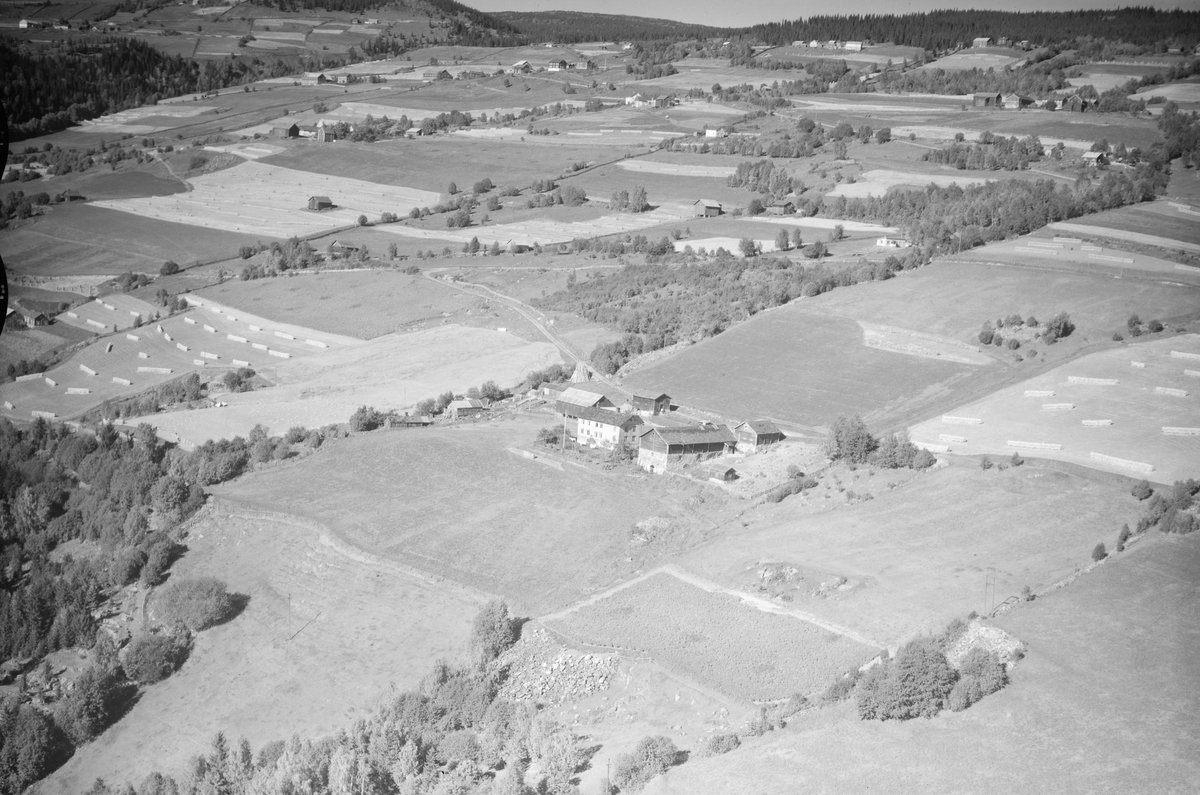Solheim gård, Øyer, 1952, Et stort, lyst toetasjes våningshus, stor driftsbygning og flere uthus. Kjøkkenhage, flaggstang, jordbruk, slåttonn, hesjing, kornstaur, flere gårder oppover i lia. Hovsåa renner forbi på venstre side.
