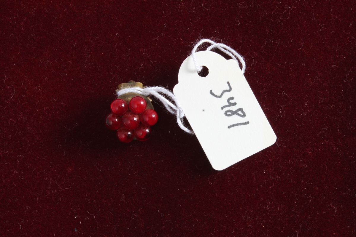 Gitt av Torill Lerdalen Hùser (f.1946).
Det er 1/2 par ørepynt. Den andre halvdelen er borte fra giver. Det er en clips øredobb med rød perle.