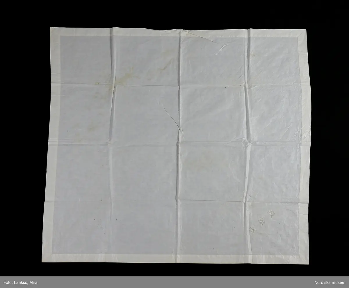 Kvadratiskt kläde av vit tät och fin bomullsväv i tuskaft, 3,7 cm bred handsydd fåll runtom. Tvärs över ena hörnet märkt KID med vitt bomullsgarn i klumpsöm.
Klädet stärkt och glättat och verkar aldrig vara tvättat ( syns på märkningen).
/Berit Eldvik 2010-06-28