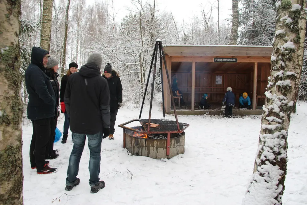 Foto av folk som griller og koser seg ved bålplassen og barn leker i gapahuken.