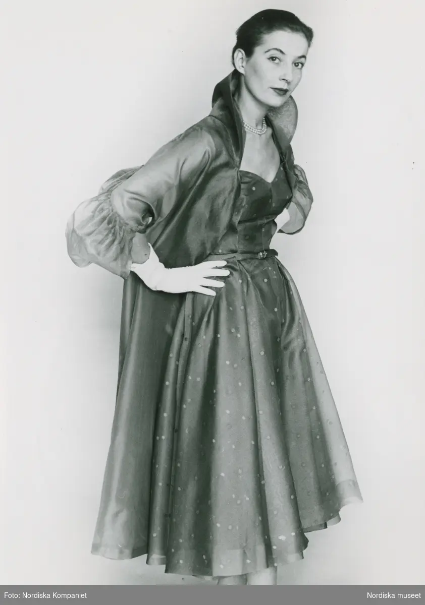 Modell i prickig klänning, kappa, tvåradigt pärlhalsband och handskar. "Giovanelli, Italiana".