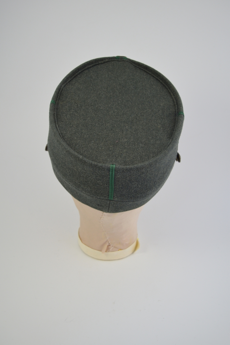 Uniform i tre deler: jakke, lue og patronveske. Innsvinget jakke med fire lommer,enkelt spent,nedbrettet krage. Bøtteformet lue med distinksjoner. Svart lærbrem og svart lærrem som går over bremmen. Kvadratisk patronveske i grønt lerretsstoff, med stor svar trykknapp foran.