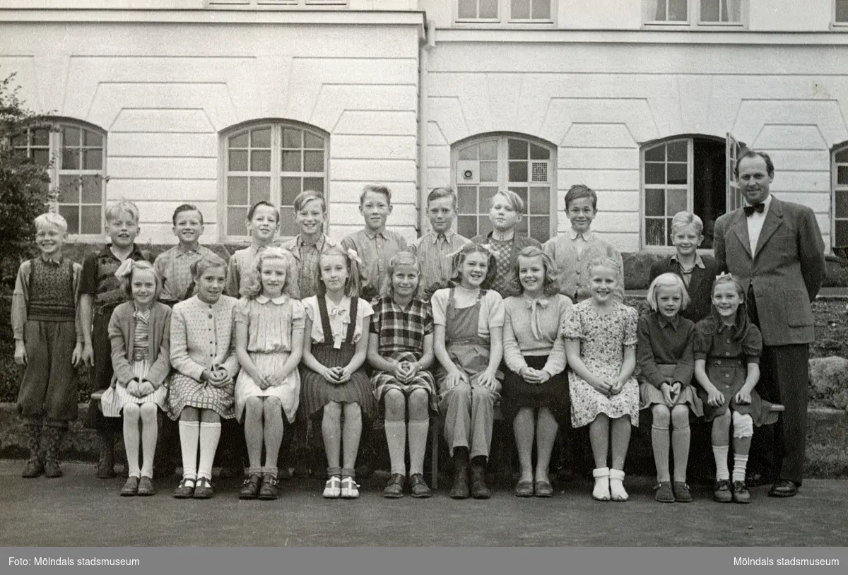 Elever (5:e klass) och magister Per Hasselgren står uppställda utanför Krokslättsskolan år 1949. Ninnie Johansson (gift Martin) sitter längst till vänster med uppsatt hår och stor rosett. Hennes familj bodde i ett flerfamiljshus som låg mittemot skolgården.