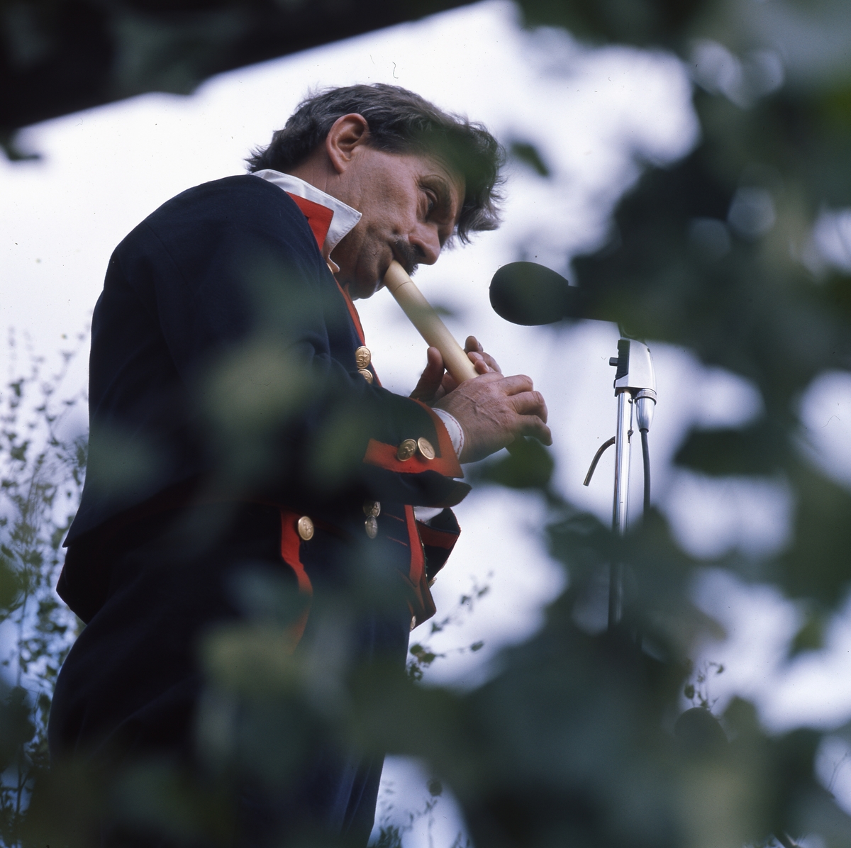 "Afton på Ängratörn". En man iklädd folkdräkt står framför en mikrofon och spelar flöjt.