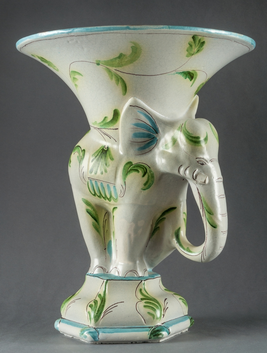 Fruktskål i form av en elefant med en trattformad skål på ryggen. Tillverkad vid Bo Fajans, design Allan Ebeling. Dekor i blått och grönt mot vit botten.