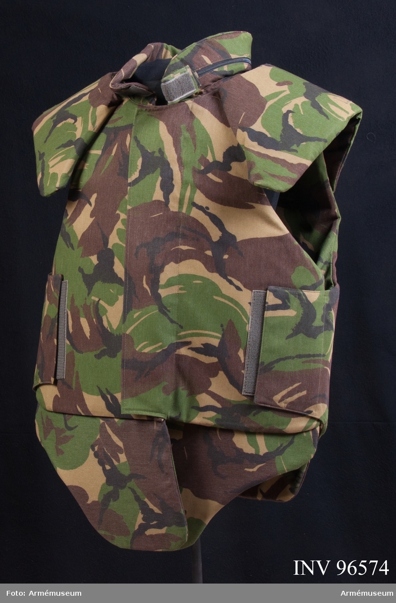 Kroppsskyddsväst i Woodland-camouflage. På etiketten i skyddsvästen står följande: "LBA Wahler GmbH. D-8355 Hengerberg. Schwanenkirschnerstr. 20.Body Armour -90. Musterweste Typ1".