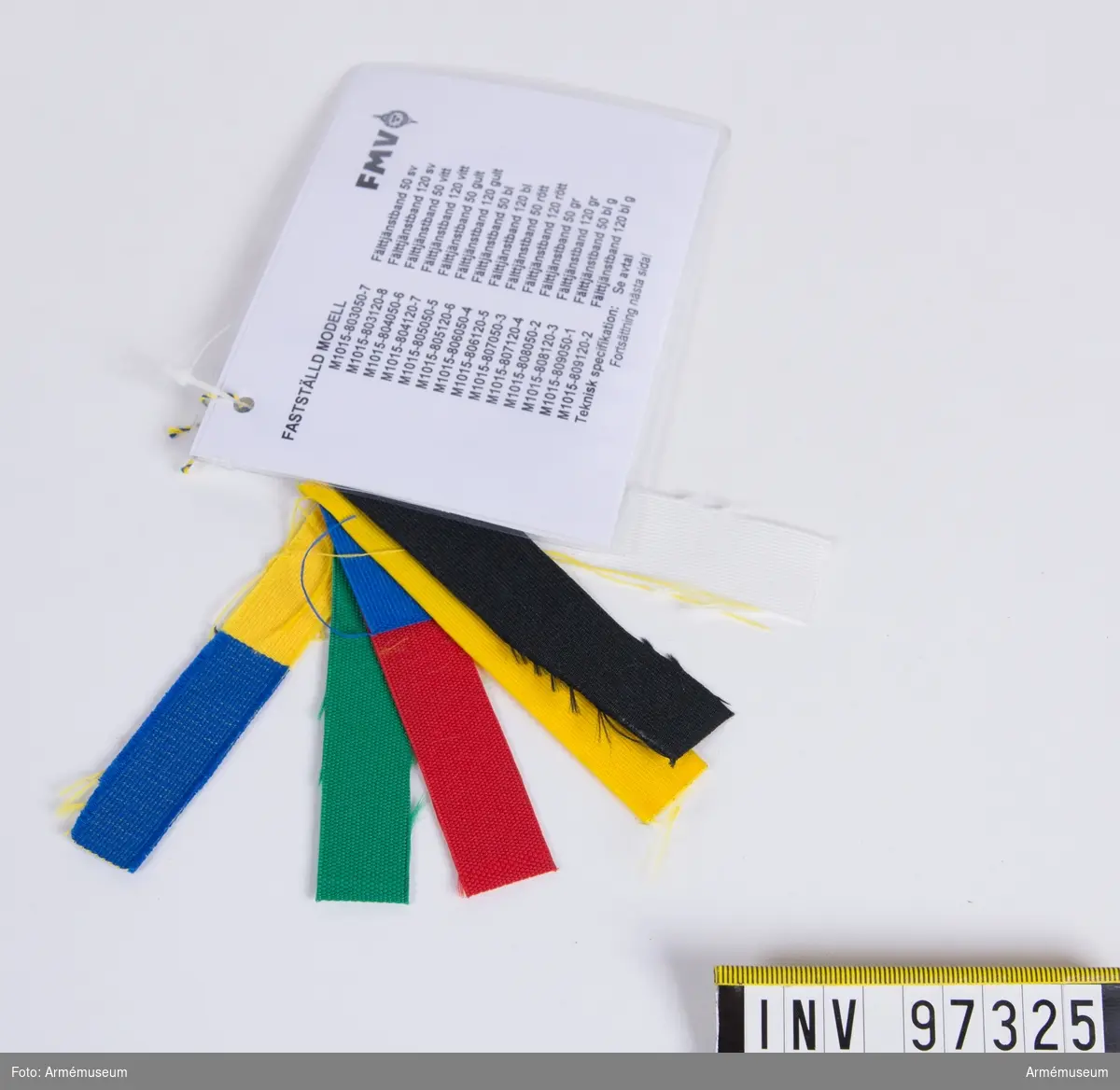 Knippe med prov på band i olika färger. Varje färg har eget M-nummer. På den vidhängande modellappen anges alla M-nummer samt att teknisk bestämmelse finns i avtalet. Lappen är underskriven 1999-01-14 av Hans Norlén och Roger Strömstedt.