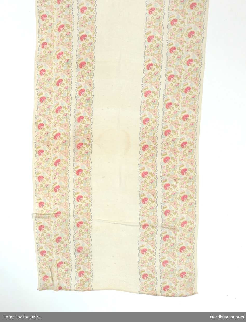 Lång schal av tunn silkecrépe, vit med bårder längs båda långsidorna med tryckt mönster med orientaliskt påverkat blommönster i kantig stil i pastellfärger av rosa, ljusgrönt, gult och ljusblått. Hansydda smala fållar i kortsidorna.
Har tillhört småskollärarinnan Emma Göransson från Kabbarp född 1879. Se även en samling klänningar mm. som visar hennes intresse för kläder och mode.
/Berit Eldvik 2012-01-13