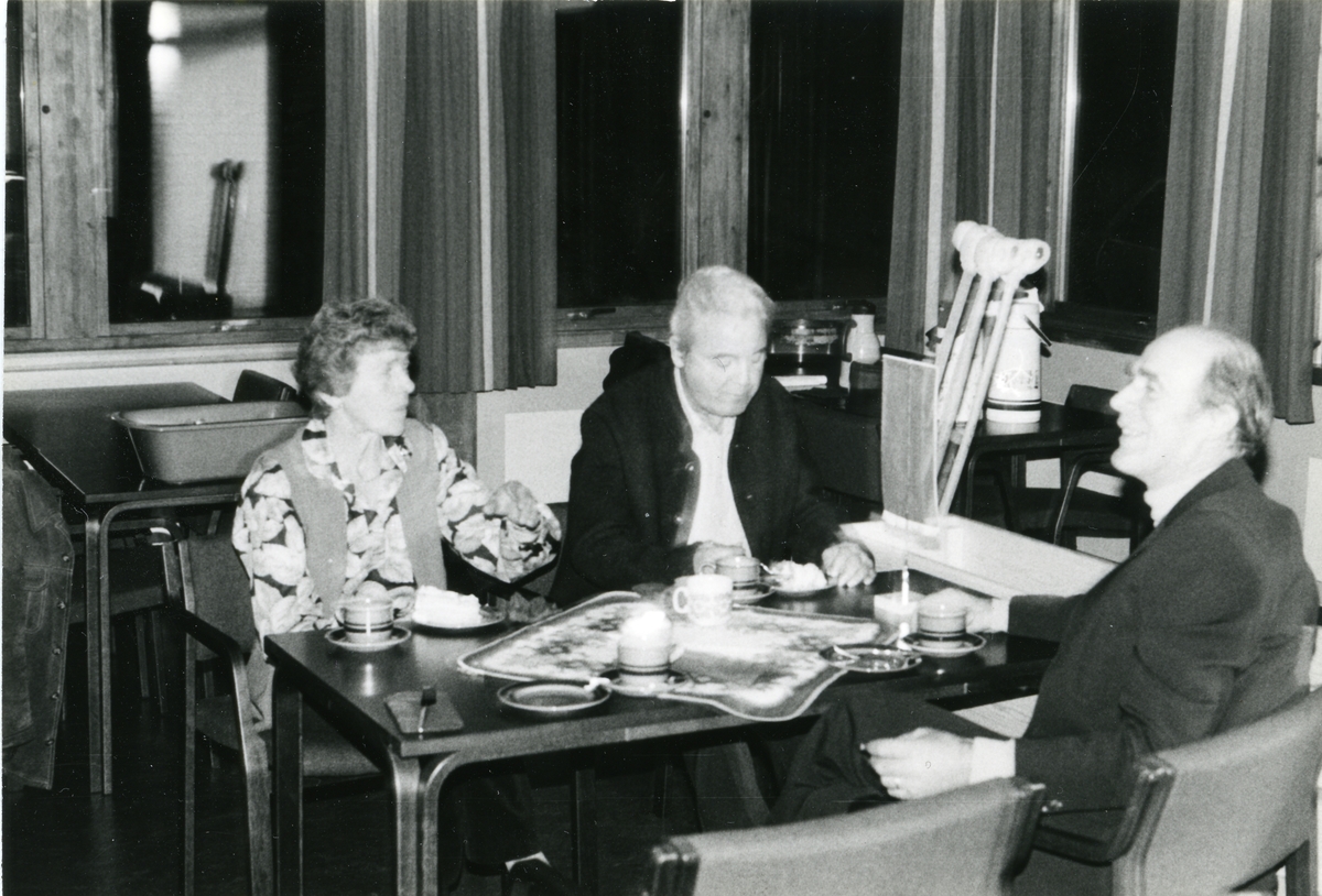 En kvinne og to menn sitter og drikker kaffe ved et bord.