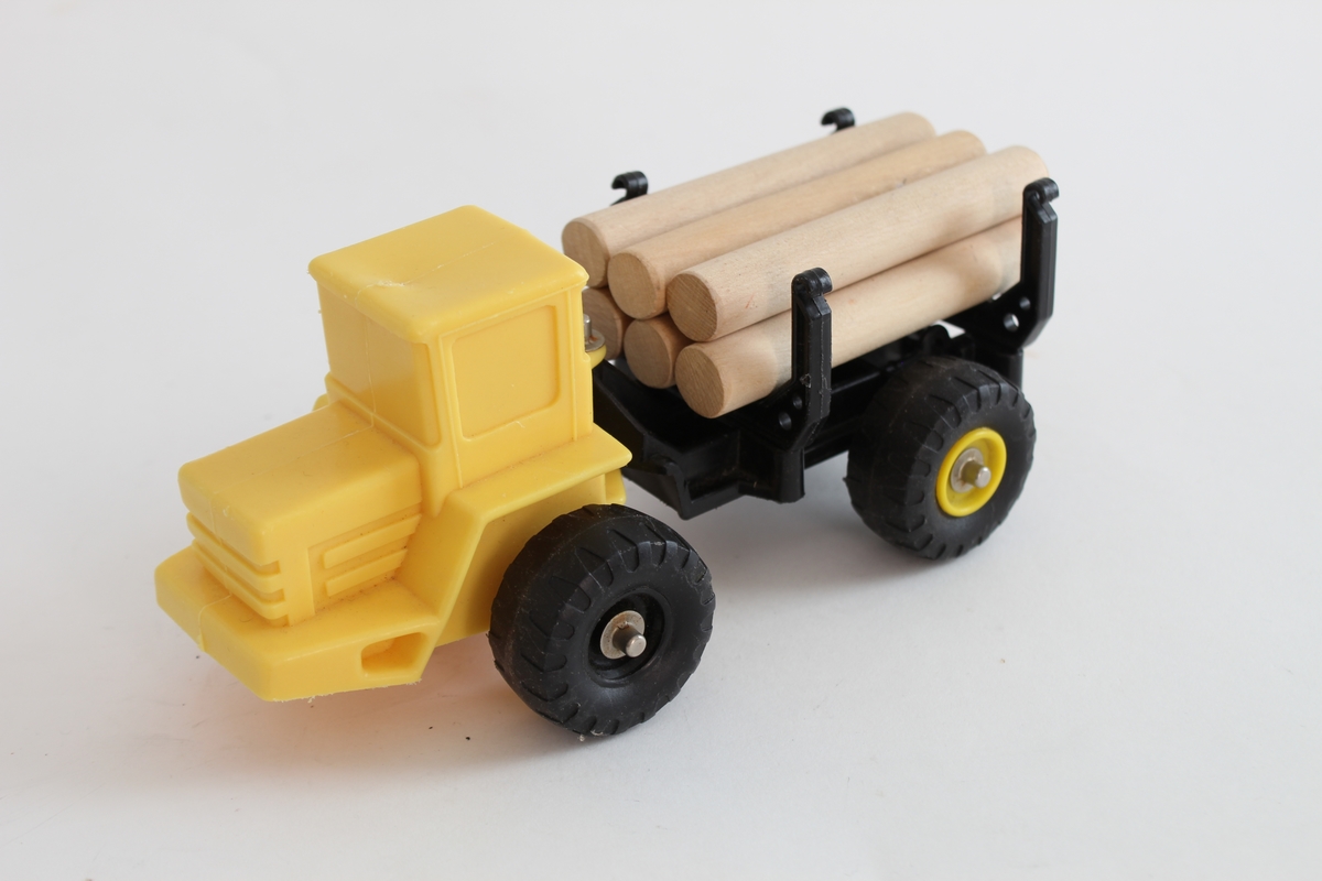 Giver. Bjørn Sverre Hol Haugen (f.1972).
En gul traktor i plastikk, med en svart henger og 6 trepinner som etterligner på tømmer.