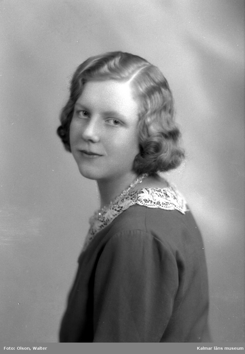 Ateljébild på en kvinnna i halsband och ondulering. Enligt Walter Olsons journal är bilden beställd av Astrid Johansson.