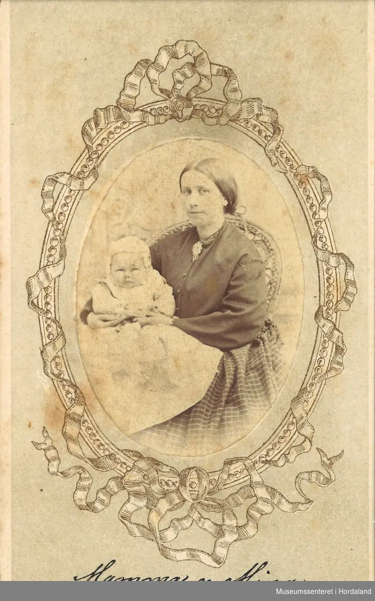 halvfigur fotografi av ung mor med spebarn på fanget. Mora sit på ein korgstol.
