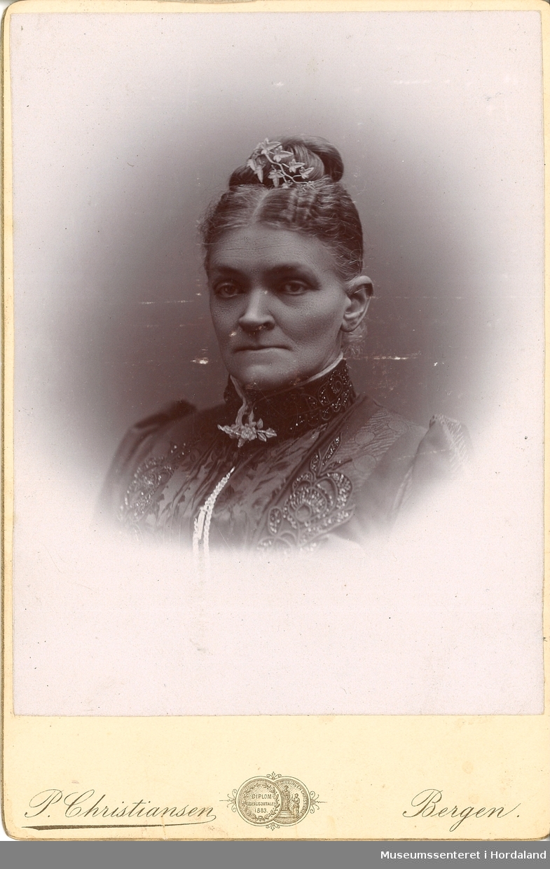 portrettfotografi av kvinne med oppsatt hår, mørk kjole med perlebroderi og bladsmykke i halsen og  håret