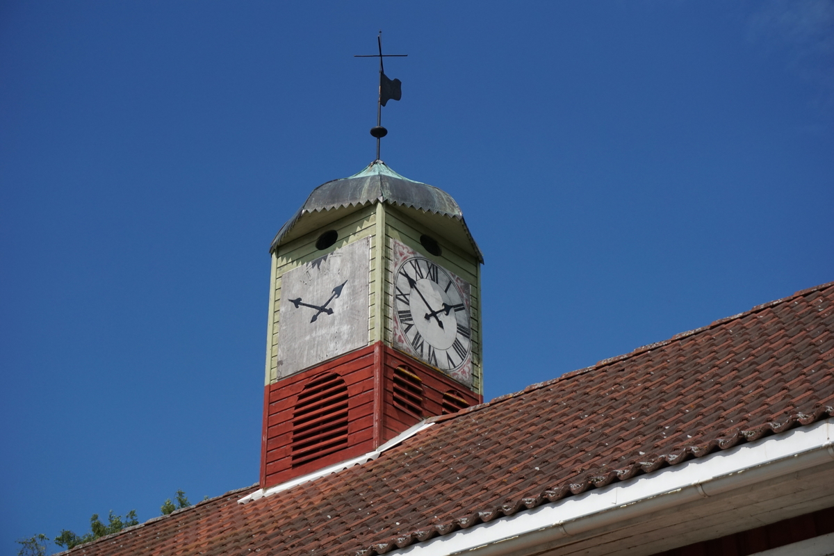 Hovinsholm, Nes, Ringsaker. 
Lukket klokketårn med illuderte urskiver på fire sider. Klokketårnet har et lavt hjelmformet kobbertak. Tårnet er plassert på en rød sokkel.