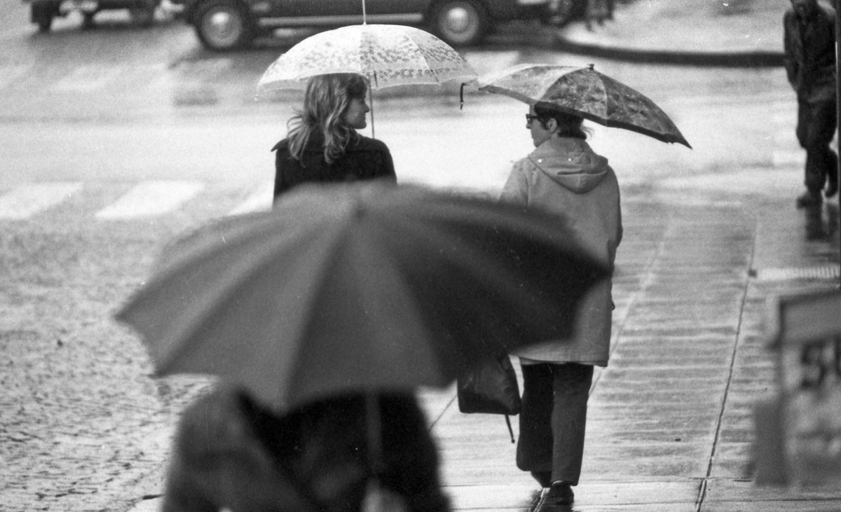 Regnværsbilder. En travel bygate med paraplybærende innbyggere som haster avsted i regnværet.