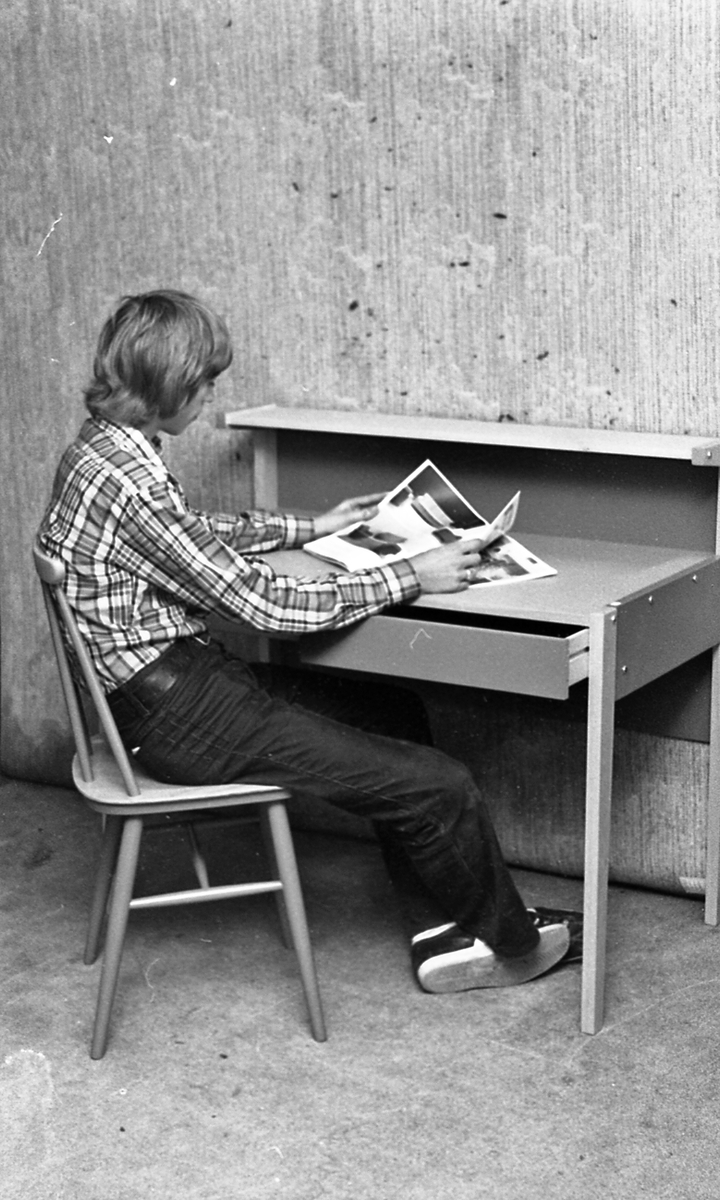 Ung mann som sitter ved pulten og leser et interiørmagasin.