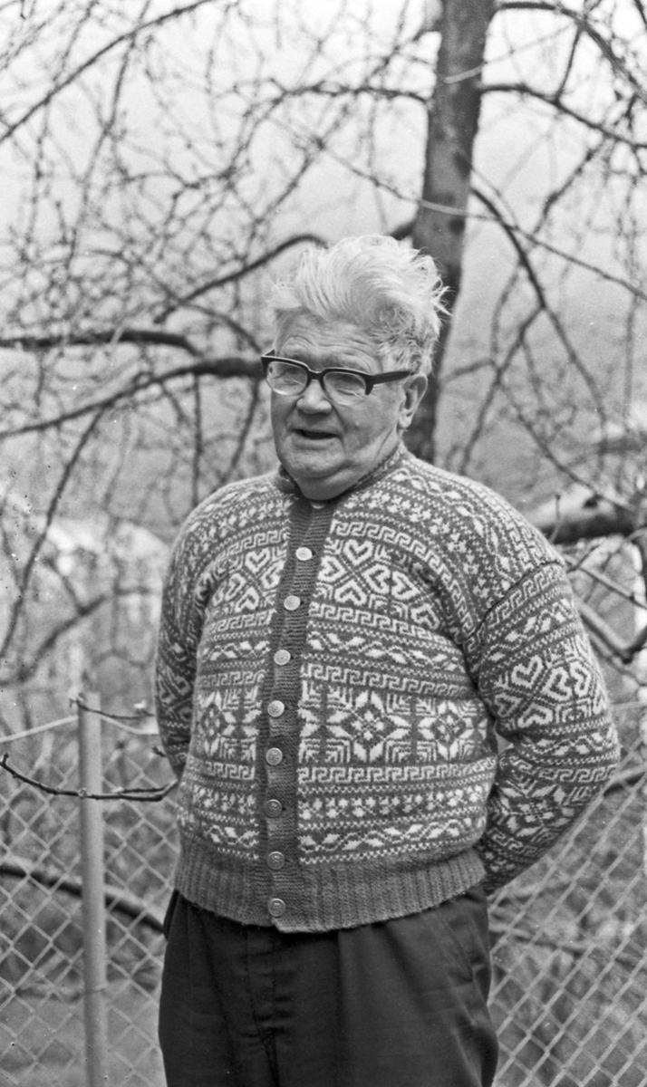 Portrett av mann med briller iført strikket kofte.