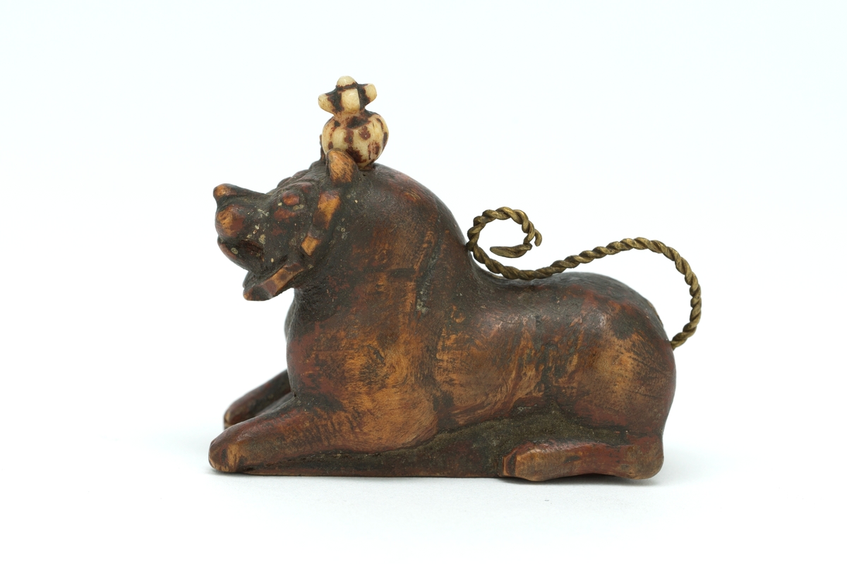 Liggende løvefigur av tre med snodd messingtrådshale. Lokk i bunnen.