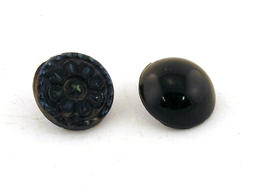 Två stycken knappar av svart glas, den ena slät den andra med blommotiv.

Enligt liggaren: Knappar av stenkol, olika storlekar.