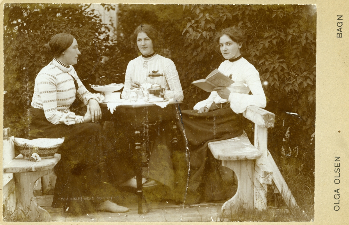 Tre kvinner sit rundt eit bord i ein hage.