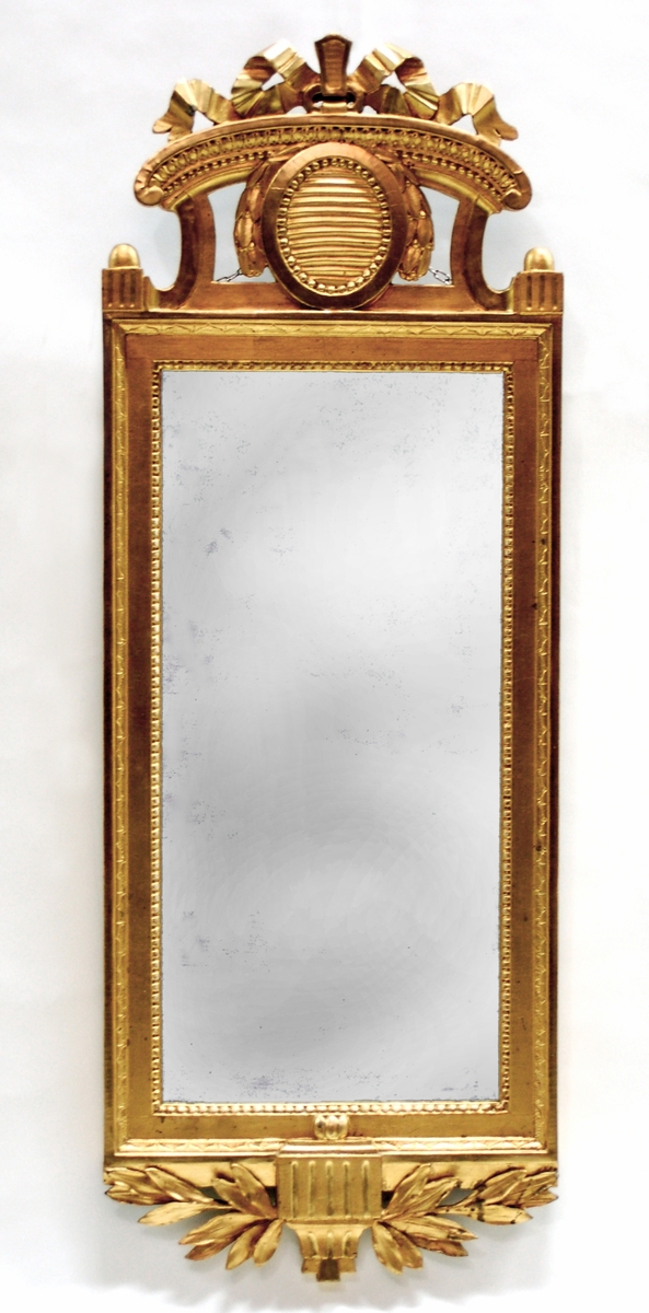 Spegel, förgylld. Långsträckt rektangulär ram med nyklassicistiska bårder. Överstycke med lagerblad.