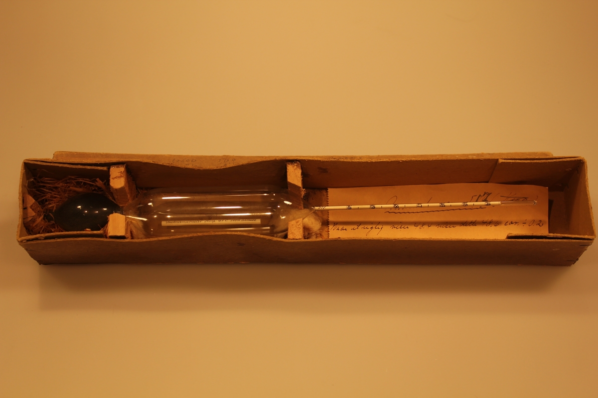 Måleinstrument for verdier i melken ved 15 grader. Det har en sylindrisk form med innsnevring to steder. Instrumentet ligger i original embalasje.