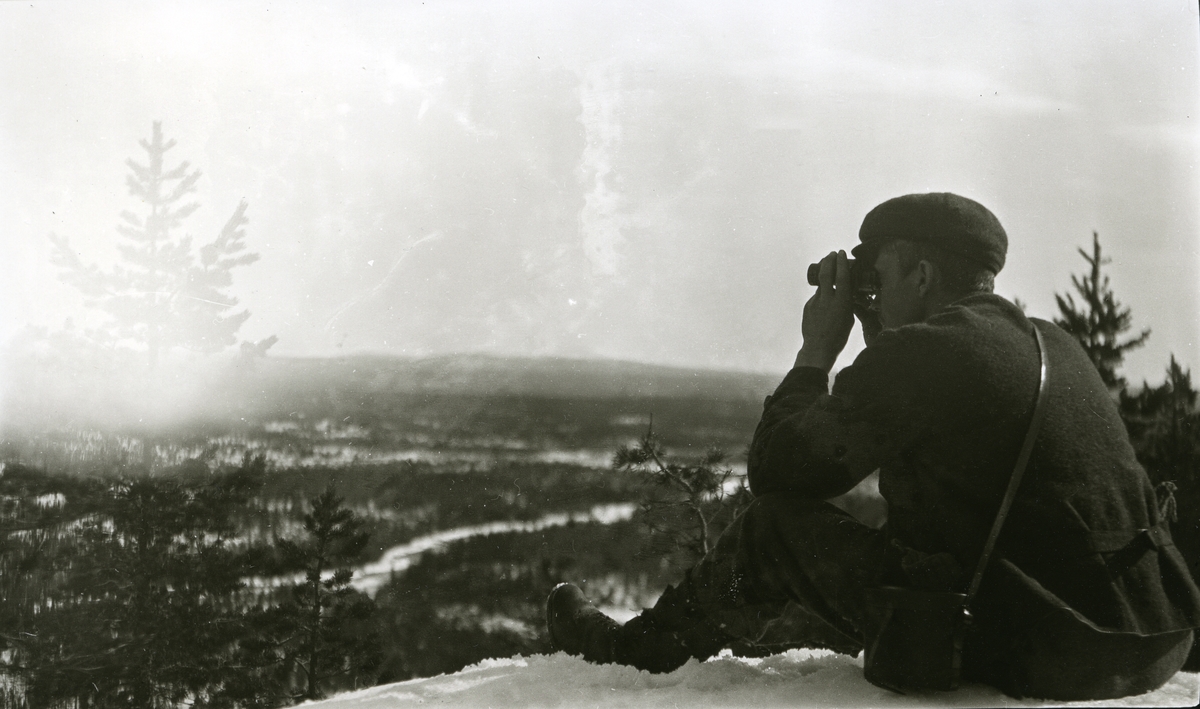 Mann med kikkert sittende på toppen av Buskneshøgda, Galåsen, speider mot grensefjella i øst.