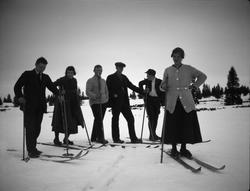 En gruppe på to kvinner i skjørt og 4 menn er ute på skitur.