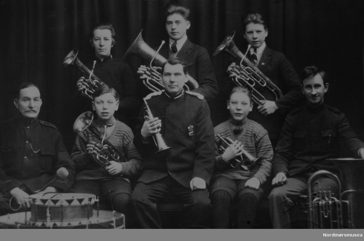 Lite musikkorps med 8 medlemmer. Althorn, baryton, tuba, trompet, tromme. 2 voksne, 4 ungdommer, 2 barn. Kristiansund 1920-tallet. Aspirantgruppe?  Nordmøre museums fotosamling.