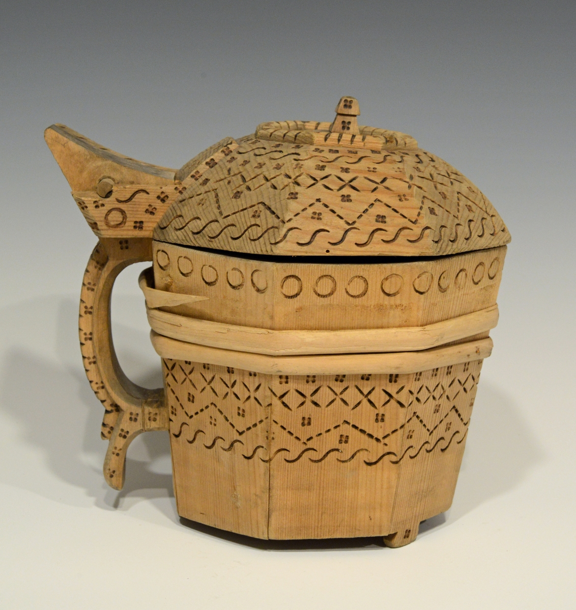 Fra katalog: Ottekantet smørkande og stav med hank og laak og tre smaa føtter, utvendig svimerket og en slynget ring oppe paa laaket, indvendig
rik rosette. Under staar brændemerket: A OSS 1823,