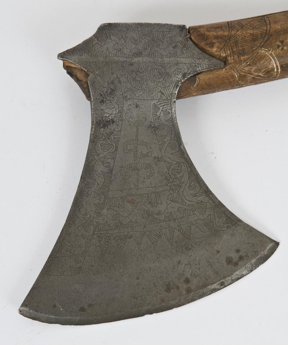 Asymmetrisk blad med lang øvre spiss og kortere nedre spiss.
Bladet er tynt, med påsmidd noe tykkere egg.
Øksehammeren har skaftehull og fliker.
Smedmerke formet som et skjell. Øksen har etset rankedekor på begge sider.
Skaftet er svakt krummet. Skaftet er merket på ryggen SON ANO 1700.Skaftet har skåret dekor i felter.