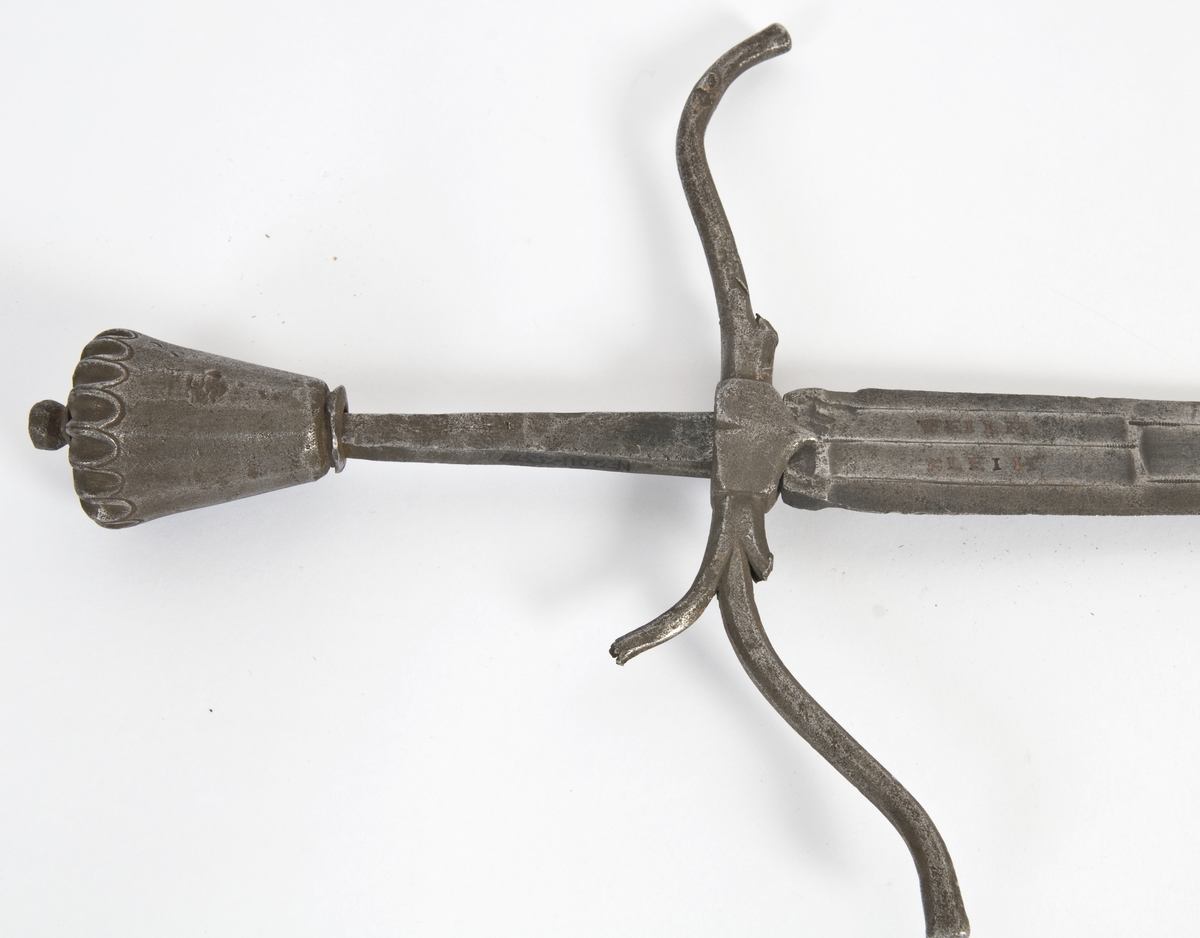 Vaseformet knapp som er fasetert og med skulpturert topp, samt nitteknapp.  
Grep mangler.
S-formede parerstenger, resten av grepet mangler.
Klingen har 6-kantet tverrsnitt med 3 korte blodrender og avbrukket spiss.
På begge sider av klingen løpende ulv, pluss innskripsjon: WHIM og KLEIH.
Innskripsjoner og ulver er innlagt med kobber.