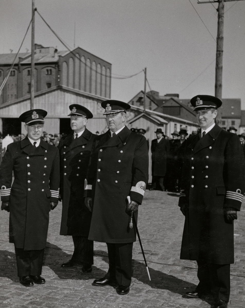 Konteramiral Samuelson och Kommendörkapten Lind af Hageby står på en öppen plats tillsammans med ytterligare två högre militära tjänstemän. I bakgrunden syns civilklädda åskådare och byggnader.