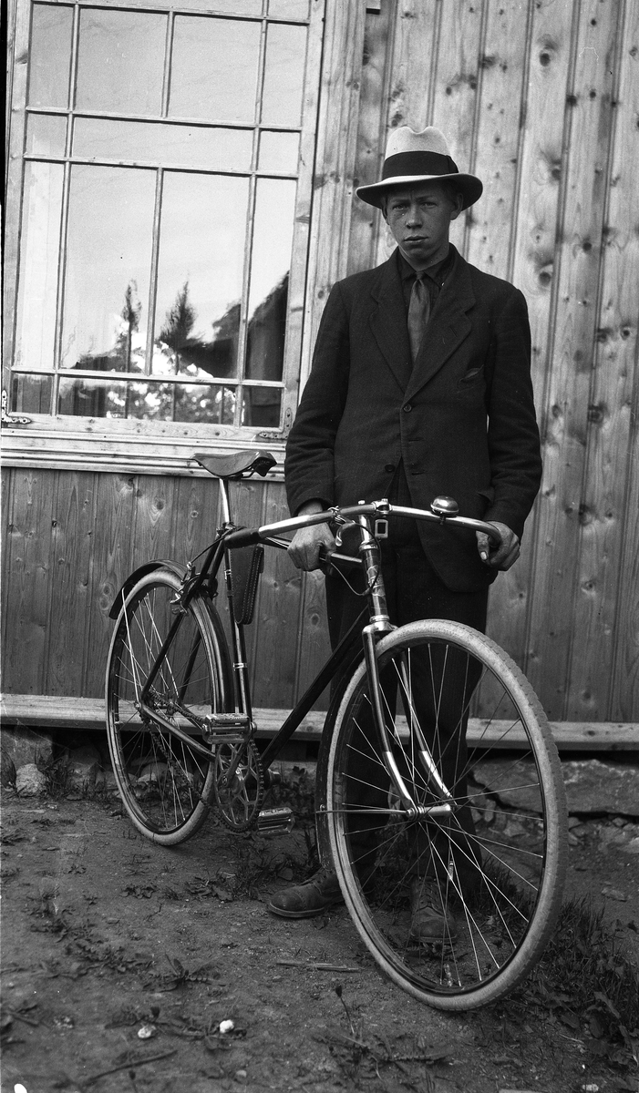 Uidentifisert ung mann med sykkel foran en husvegg.