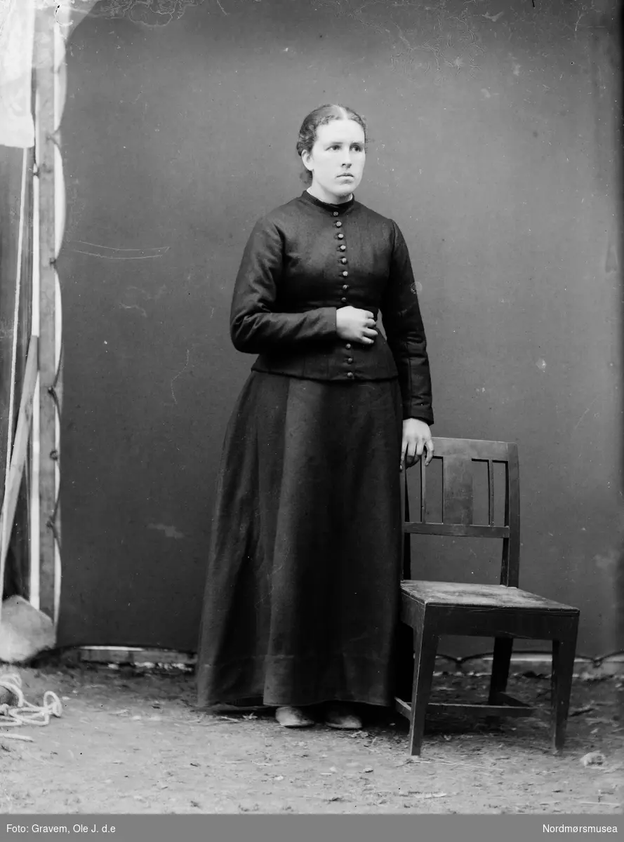 Portrettfoto i helfigur av kvinne i atelier stående ved en stol.