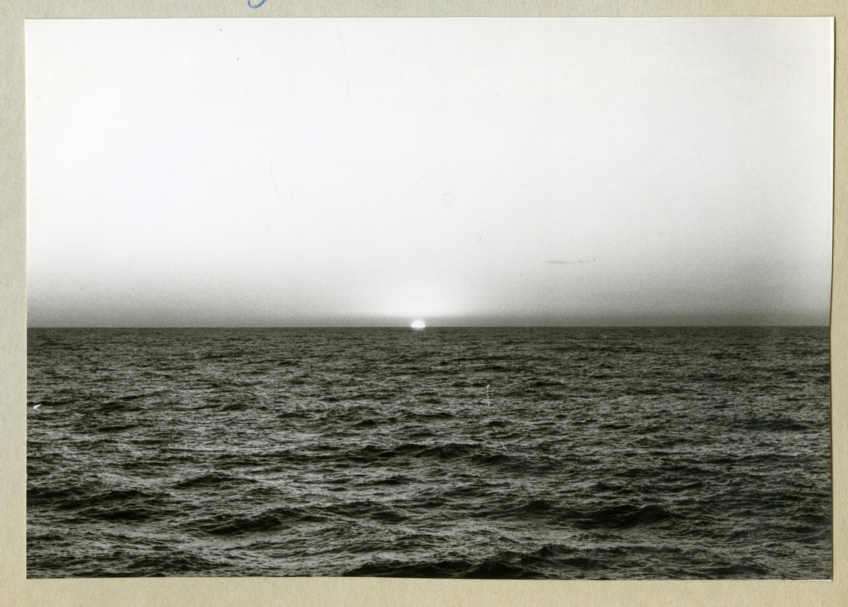Bilden föreställer en solnedgång i horisonten, där en klar himmel möter hav. Bilden är tagen under minfartyget Älvsnabbens långresa 1966-1967.