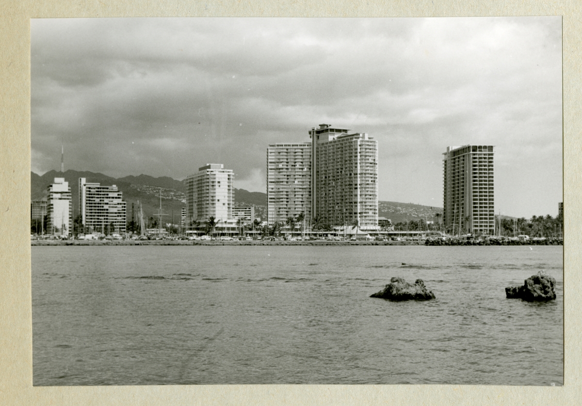 Bilden föreställer ett berglandskap och bebyggelse med höghus längs med kustlinjen. Framför husen ligger även ett stort antal segelbåtar förtöjda. Bilden är tagen under minfartyget Älvsnabbens långresa 1966-1967.