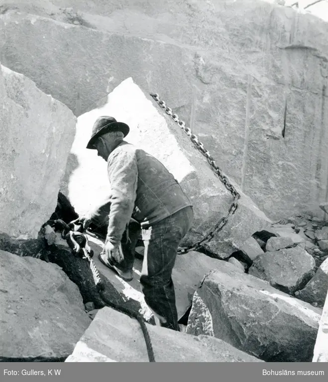 Stenhuggare förbereder för flyttning av ett stenblock, runt blocket är en kätting dragen