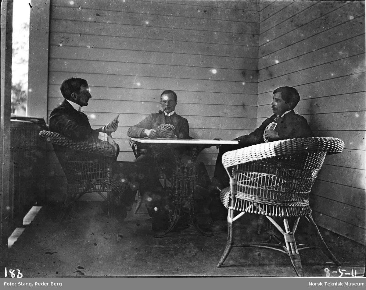 Tre menn spiller kort på verandaen på Casino