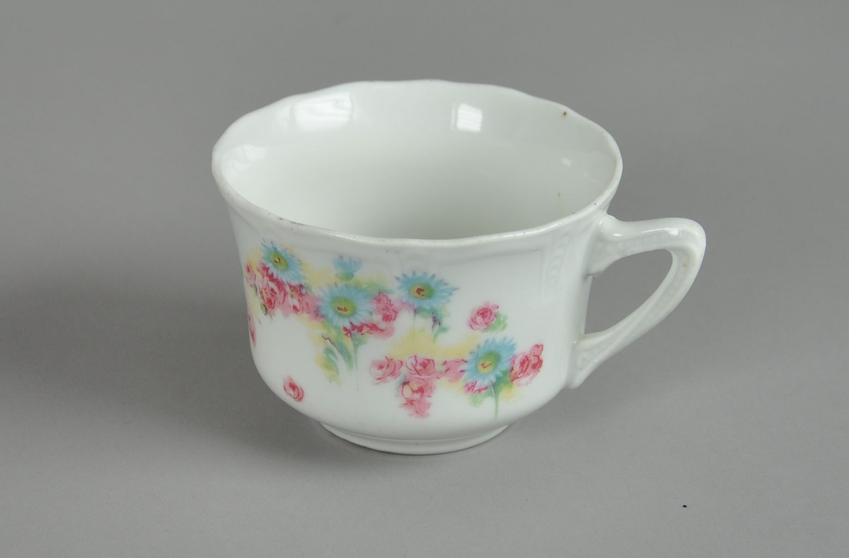 Kopp til servise, av glassert keramikk. På hanken og ved munneranden er det preget dekor. På koppen er det malt dekor med motiv av blomster.