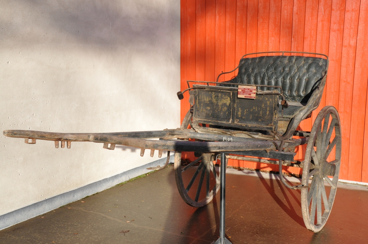 2-hjuls vogn for én hest til persontransport. Sete utført som rammeverk med fyllinger hvilende på jernbeslag.